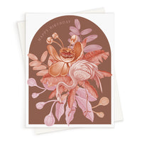 A greeting card with an arched illustration of pink and coral flowers with leaves on a brown background and "Happy Birthday" text, illustrated by Lisel Ashlock.