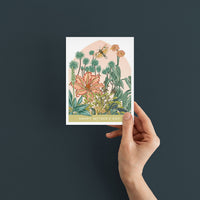 Hand holding a Mother's Day greeting card featuring illustrated botanical garden with flowers and butterfly. Illustrated by Lisel Ashlock.