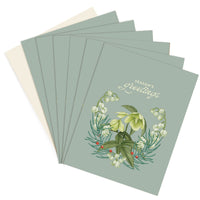 A fan-spread display of season's greetings cards featuring sage green covers with white hellebores and holly berries. Illustrated by Lisel Ashlock.