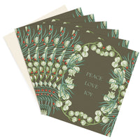 Stack of holiday greeting cards with olive green background, white bell flowers, red berries, and green foliage forming a wreath around "Peace Love Joy" text. Illustrated by Lisel Ashlock.