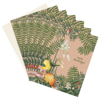 A fanned stack of holiday greeting cards featuring botanical illustrations of citrus fruits, berries, and ferns on a blush background. Illustrated by Lisel Ashlock.