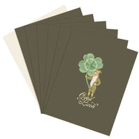 Stack of green greeting cards with leprechaun holding four-leaf clover and "Good Luck" text. Illustrated by Lisel Ashlock.