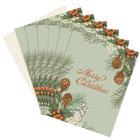 A fan of holiday greeting cards featuring holly branches, pinecones, berries, and a hare with "Merry Christmas" text. Illustrated by Lisel Ashlock.