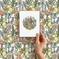 Hand holding blank greeting card featuring circular desert succulent illustration over repeating cactus pattern background. Illustrated by Lisel Ashlock.