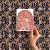 A hand holding a Happy Birthday greeting card featuring illustrated flamingos and flowers in coral and pink tones. Illustrated by Lisel Ashlock.
