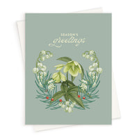 Season's Greetings card with botanical wreath of hellebores, snowdrops, and holly berries on sage green background. Illustrated by Lisel Ashlock.