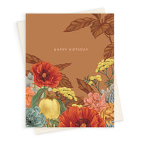 A rust-colored birthday greeting card featuring illustrated red poppies, yellow flowers, a lemon, and autumn leaves. Illustrated by Lisel Ashlock.