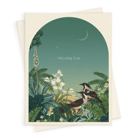 Greeting card with arch-shaped illustration of birds in a moonlit garden with white flowers and ferns, text reads "Missing You." Illustrated by Lisel Ashlock.