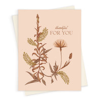Greeting card with botanical illustrations in brown and gold tones on blush background reading "thankful FOR YOU" Illustrated by Lisel Ashlock.