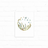 Watercolor illustration of grasses and wildflowers arranged in a circular wreath with blue-green leaves floating above. Illustrated by Lisel Ashlock.