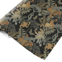 A roll of gift wrap featuring monkeys, snakes, flowers and butterflies in gold, gray and tan on a black background. Illustrated by Lisel Ashlock.