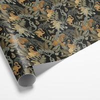 Rolled gift wrap with botanical pattern featuring golden monkeys, cream ferns, and butterflies on dark background. Illustrated by Lisel Ashlock.