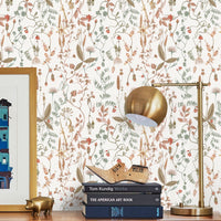 A wooden desk displays books and brass decor against Sonoma Wallpaper in white featuring botanical illustrations by Lisel Ashlock.