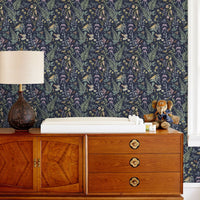 A mid-century wooden dresser with changing table top against Secret Garden wallpaper featuring botanical illustrations by Lisel Ashlock.