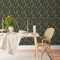 Secret Garden Wallpaper in ebony covers a dining room wall behind a wooden table and rattan chair. Illustrated by Lisel Ashlock.