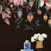 Dark floral wallpaper mural featuring hanging illustrated flowers above wooden shelf with books, blue jar, and white peonies. Illustrated by Lisel Ashlock.