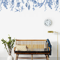 A mid-century crib with cream bedding beneath a blue floral wall mural in a minimalist nursery. Illustrated by Lisel Ashlock.