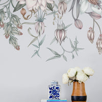 Canopy Mural in Cloud Grey featuring botanical illustrations displayed above wooden shelf with books, blue ginger jar, and white flowers. Illustrated by Lisel Ashlock.