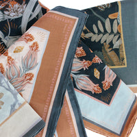 Folded silk cotton scarves in botanical prints featuring flowers and leaves in terracotta and teal. Illustrated by Lisel Ashlock.
