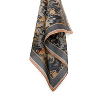 Charcoal silk cotton scarf with gold, bronze, and cream botanical and animal motifs, rolled display. Illustrated by Lisel Ashlock.