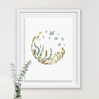 Watercolor illustration of wildflowers and grasses arranged in a circular design with blue butterflies above, framed in white. Illustrated by Lisel Ashlock.
